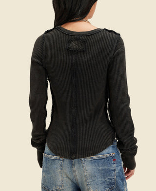 A woman shown from the back wearing a black textured long-sleeve top and blue jeans against a plain white background.
