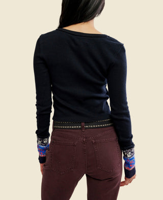 A woman wearing a black long-sleeve knit noa cardigan from free people with a colorful vertical patterned placket and matching patterned cuff trim, paired with dark brown pants and a studded belt, against a plain white background.