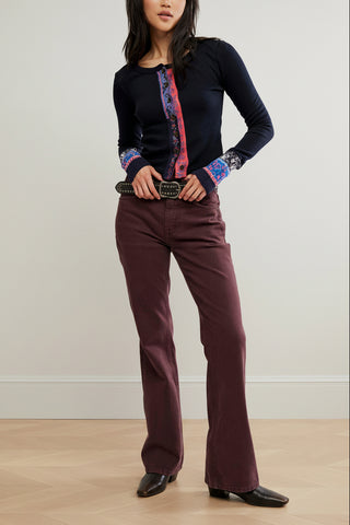 A woman wearing a black long-sleeve knit noa cardigan from free people with a colorful vertical patterned placket and matching patterned cuff trim, paired with dark brown pants and a studded belt, against a plain white background.