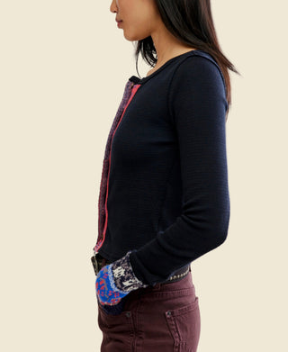 A woman wearing a black long-sleeve knit noa cardigan from free people with a colorful vertical patterned placket and matching patterned cuff trim, paired with dark brown pants and a studded belt, against a plain white background.