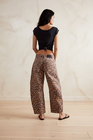 A model shown from the back wearing wide-leg leopard print pants, a black cropped tie-front t-shirt, and black sandals against a plain white background.